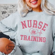 a woman with blonde hair wearing a grey sweatshirt that says nurse in training on it