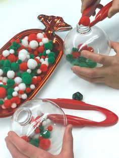 two hands are holding scissors near a glass bowl filled with pom - poms