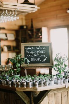 a wooden table topped with lots of cups filled with plants and greenery next to a chalkboard