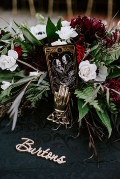 a table topped with flowers and greenery next to a metal name plate that reads bridal