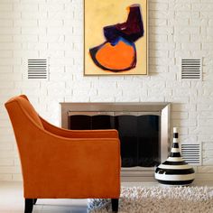 an orange chair sitting in front of a fire place next to a white brick wall