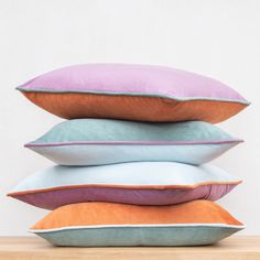 four pillows stacked on top of each other in different colors and sizes, sitting on a wooden table