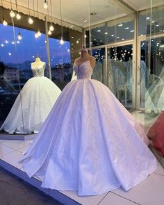 wedding gowns are on display in a store window at night, with lights hanging from the windows