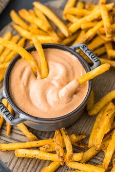 french fries with dipping sauce in a small bowl on a wooden plate next to some ketchup