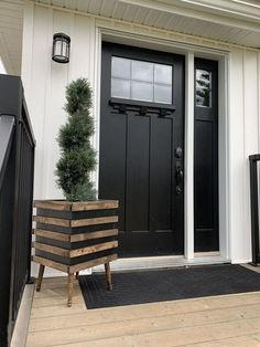 a black front door with a wooden planter on the side and a white house