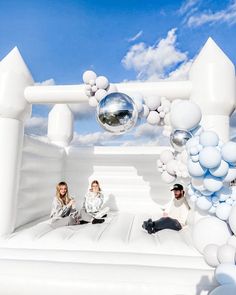 two people sitting on top of an inflatable structure with white balloons and silver balls