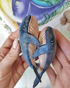 someone is holding a small blue bird with brown wings on it's back and its tail curled up in the shape of a heart