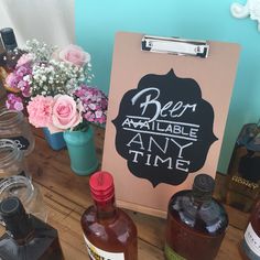 bottles of alcohol are sitting on a table next to a sign that says beer available any time