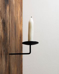 a single candle is lit on a black wall - mounted holder in front of a wooden door