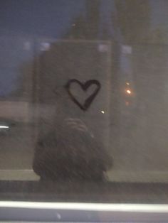 a heart drawn on the side of a bus window with rain coming in from behind it