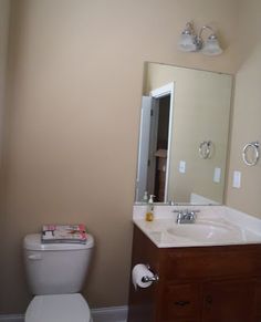 a white toilet sitting next to a wooden sink vanity in a bathroom under a mirror