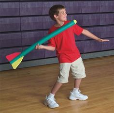 a young boy is holding a large green and yellow plastic stick in one hand while standing on a hard wood floor