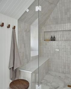 a bath room with a stand up shower next to a wooden table and white tiled walls