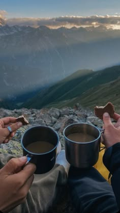 two people holding cups of coffee on top of a mountain