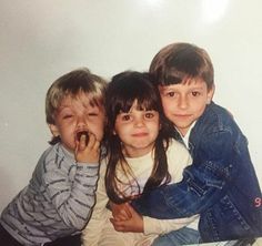 three young children sitting next to each other with their hands on their mouths and looking at the camera