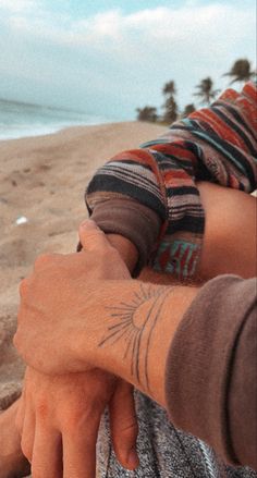 two people holding hands on the beach with waves in the background and one person has their arm wrapped around another persons hand