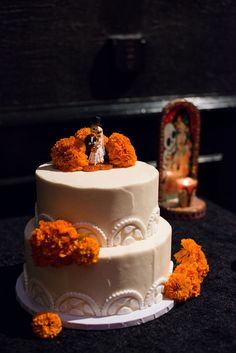 a white wedding cake with orange flowers on the side and a couple figurine on top