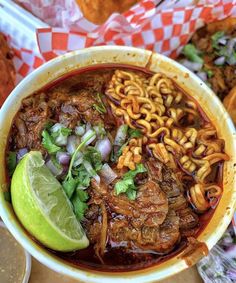 a bowl filled with noodles, meat and vegetables next to some other food on a table