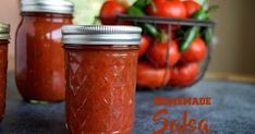 three jars filled with tomato sauce sitting on top of a table next to some tomatoes