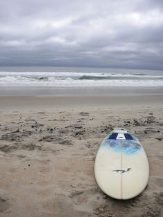 a surfboard is laying on the sand at the beach with an ocean in the background