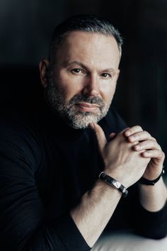 a man with a watch on his wrist posing for a photo in front of a dark background