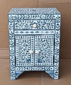 a blue and white painted cabinet on the ground next to a brick wall with a door