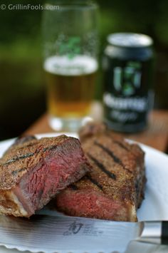 two steaks on a white plate with beer in the background