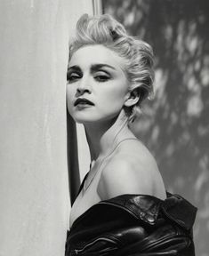 a black and white photo of a woman leaning against a wall wearing a leather jacket