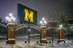 the university of michigan sign is lit up at night in front of snow covered gates