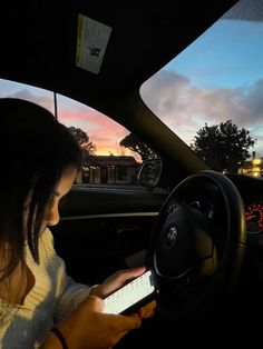 a woman is using her cell phone while driving in the car at sunset or dawn