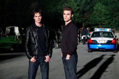 two young men standing next to each other in front of a police car on the street