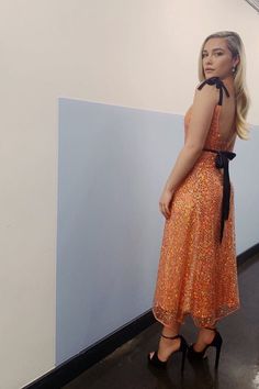 a woman in an orange dress is leaning against a wall