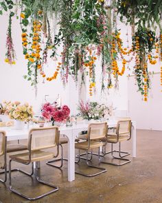 a white table with chairs and flowers hanging from it's ceiling in a room