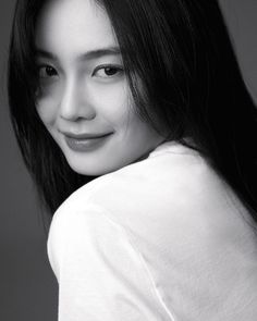 black and white photograph of a woman with long dark hair smiling at the camera while wearing a white t - shirt