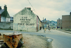 a tree stump sitting on the side of a road next to a building with a sign that says you are now entering free derby