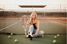 a woman sitting on the ground holding a tennis racquet next to some balls