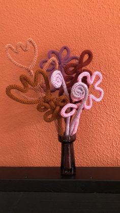 a vase filled with crocheted flowers on top of a table next to a wall