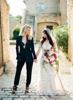 the bride and groom hold hands as they walk through an alley way in front of a stone building