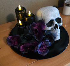 a skull sitting on top of a black plate next to some purple flowers and candles