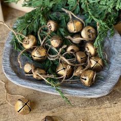 some gold bells are sitting on a wooden plate next to green leaves and pine needles