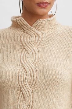 a woman wearing large hoop earrings and a beige knitted sweater with an intricate design