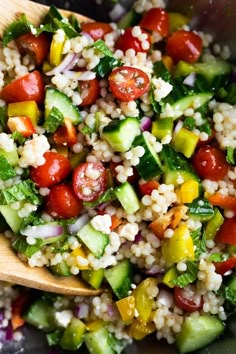 a salad with cucumbers, tomatoes, and other vegetables in a wooden spoon