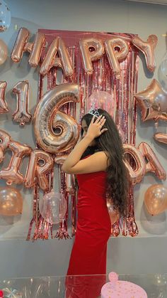 a woman in a red dress standing next to a cake and balloon wall with the words happy birthday on it