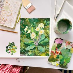 an artist's work table with flowers and paintbrushes on it, including watercolors