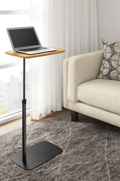 a laptop computer sitting on top of a wooden stand in front of a couch and window