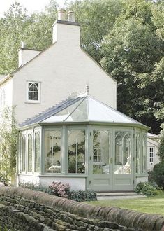 a white house with a green roof next to a stone wall