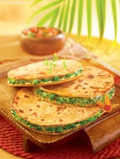 three flat breads with spinach and cheese are on a wooden tray next to a bowl