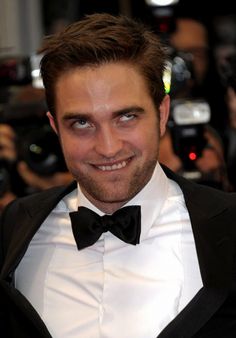 a man in a tuxedo and bow tie smiling at the camera with cameras surrounding him