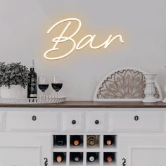 a neon sign that says bar on top of a white cabinet with wine glasses and bottles