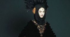 a woman wearing a black dress and headpiece with feathers on it's head